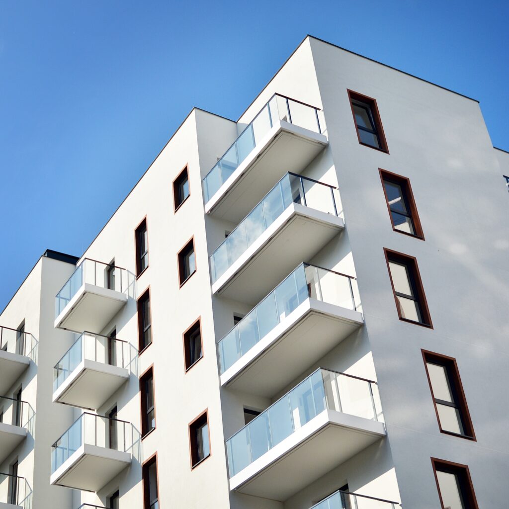 Architecture moderne : Immeuble blanc et balcons en verre Façade moderne d'immeuble blanc avec balcons en verre et cadres de fenêtres brun-rouge, sous un ciel bleu clair.