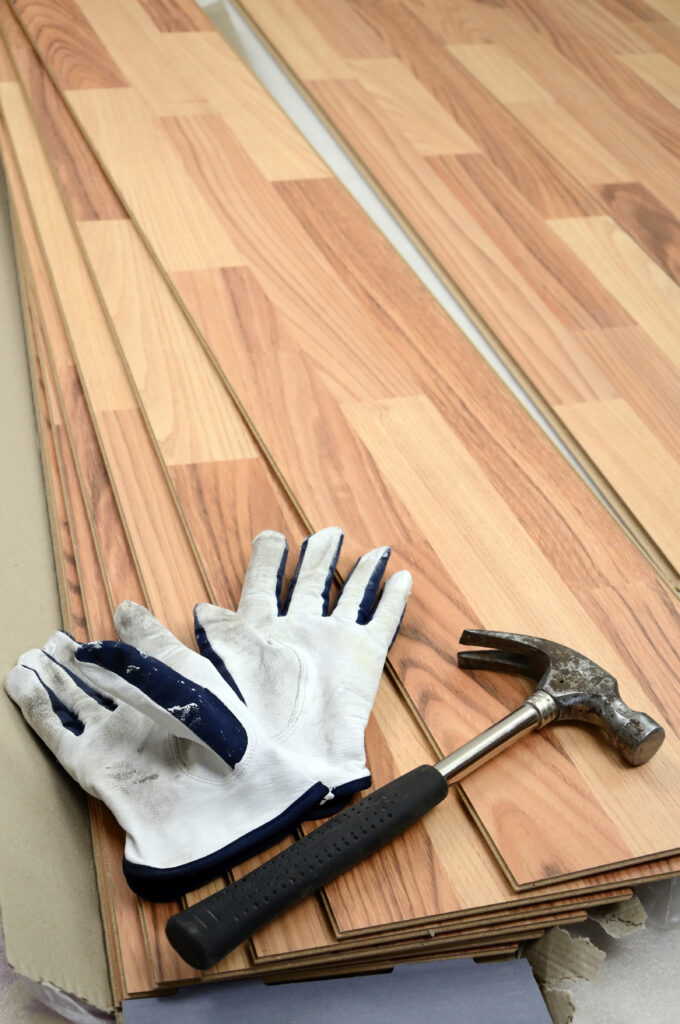 Installation Parquet Flottant : Outils et Matériaux Gants de travail blancs et usés posés sur des lames de parquet flottant en bois clair, à côté d'un marteau rouillé, prêts pour l'installation.