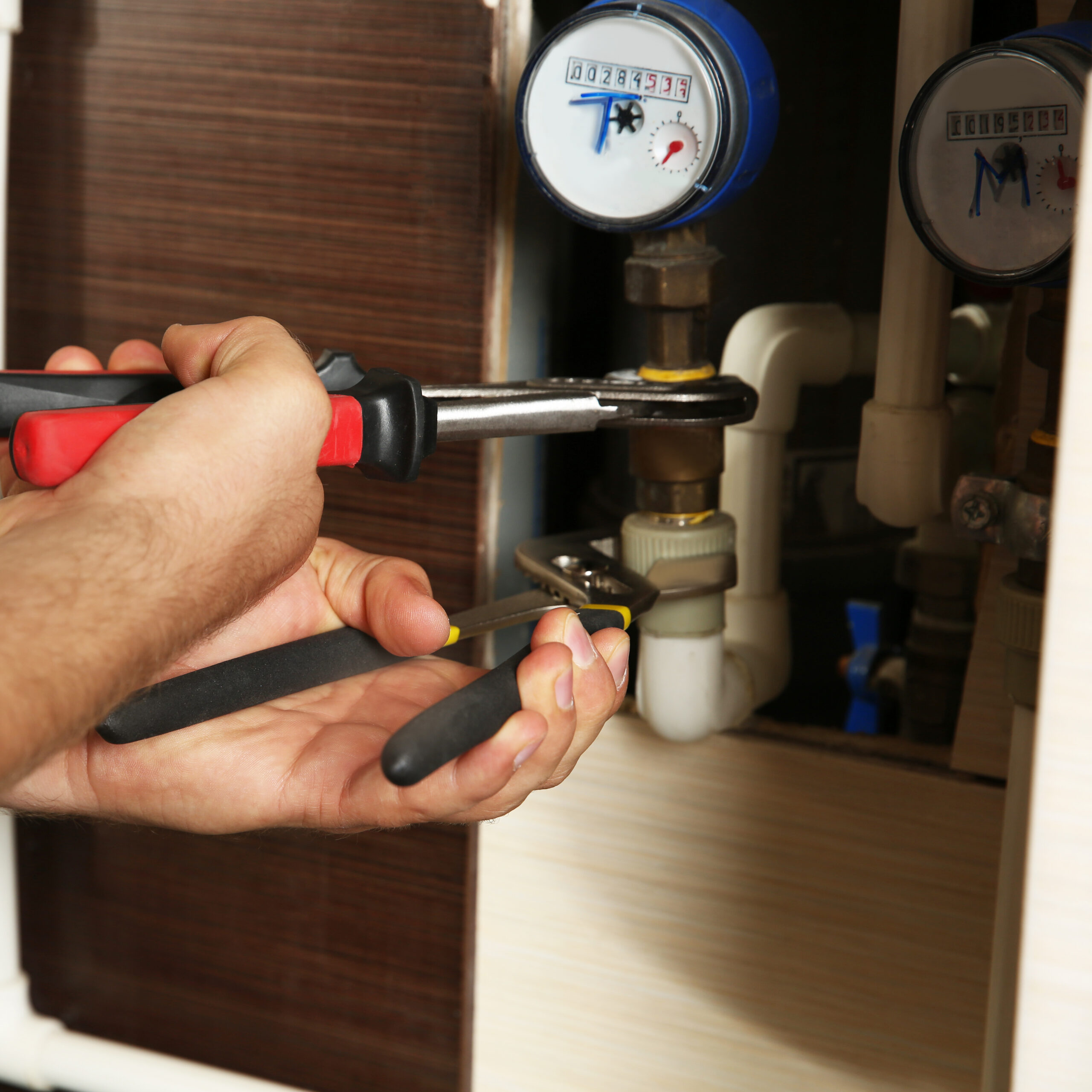 Mains utilisant une pince multiprise sur un raccord de canalisation près de compteurs d'eau (lecture 00284539).