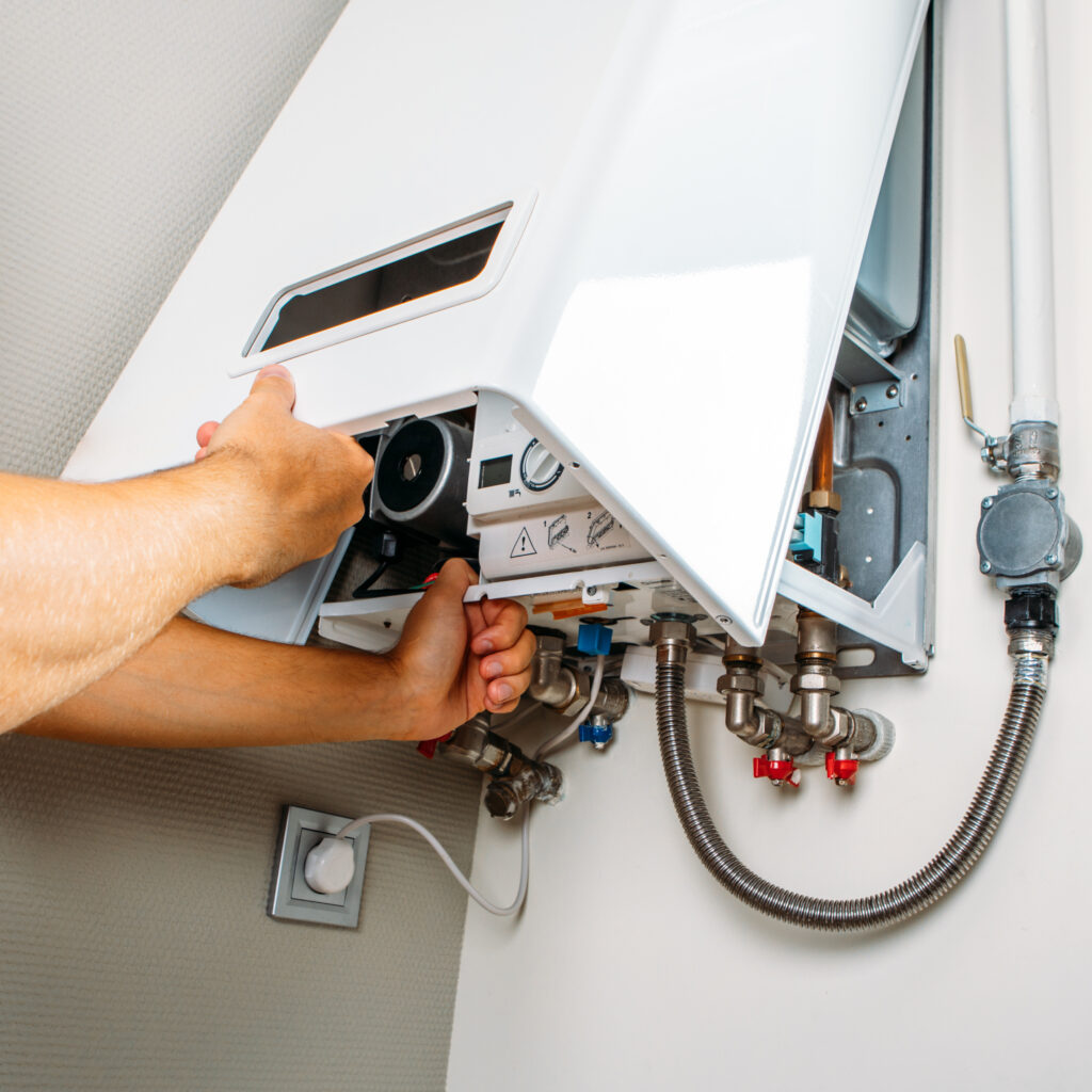 Réparation Chauffe-eau Gaz : Technicien Vérifie les Connexions Technicien ouvrant le panneau avant d'un chauffe-eau ou chaudière mural blanche, révélant des connexions et un cadran. Prise électrique visible en bas.