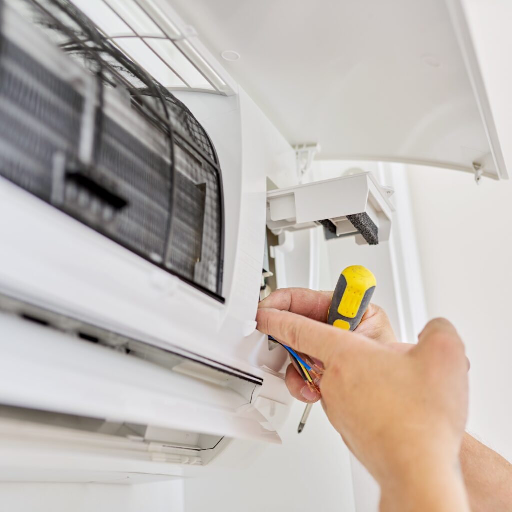 Réparation Climatiseur Split : Connexion des Fils Électriques Technicien utilisant un tournevis pour réparer les fils électriques d'une unité intérieure de climatiseur split blanc.