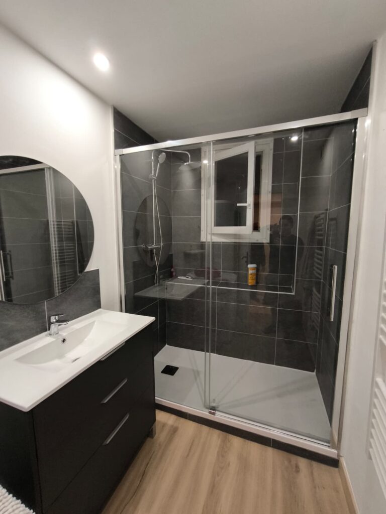 Salle de bain moderne avec douche à l'italienne carrelée gris foncé, meuble-lavabo noir et miroir rond.